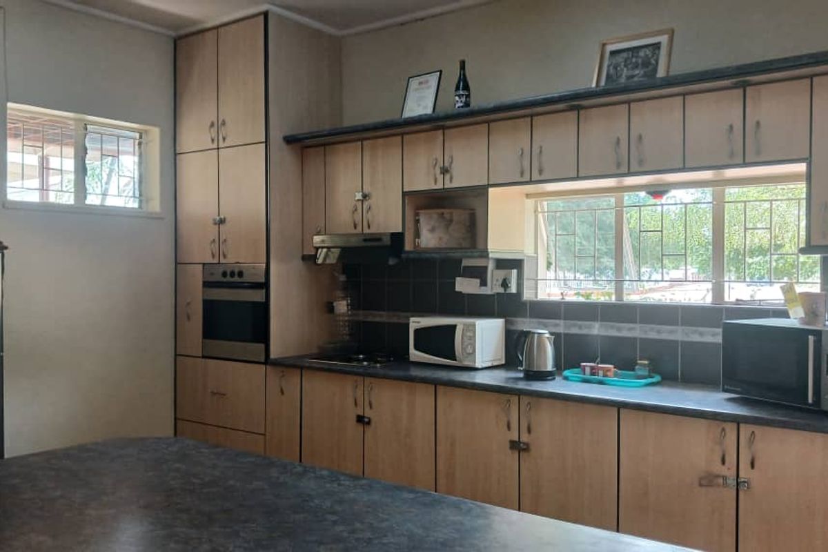 A functional kitchen featuring light wood-tone cabinetry, dark laminate countertops, a built-in oven, and an extractor fan with ample natural light.