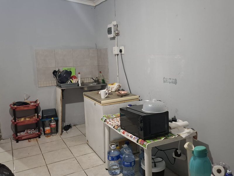A compact kitchen area featuring a stainless steel sink, tiled splashback, and ceramic floor tiles, currently requiring maintenance and cosmetic updates.