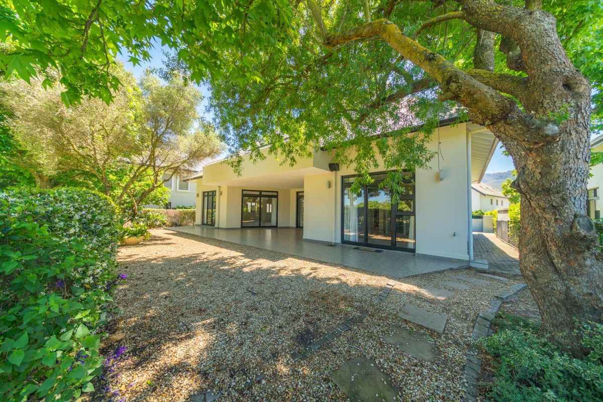 A well-maintained rear exterior view featuring a covered patio with tiled flooring, large sliding glass doors, and a landscaped gravel garden area.