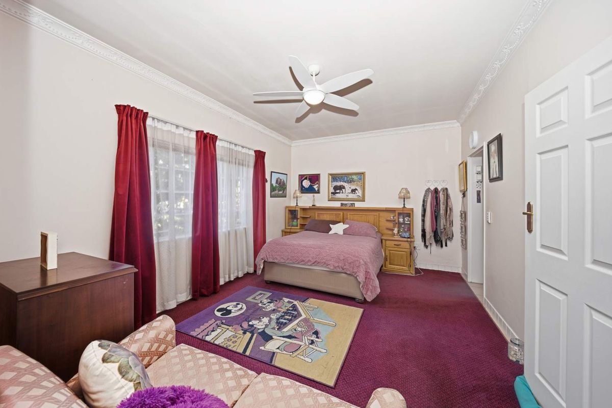 A spacious bedroom featuring crown molding, a ceiling fan, and a built-in headboard unit, offering a comfortable and functional living space.