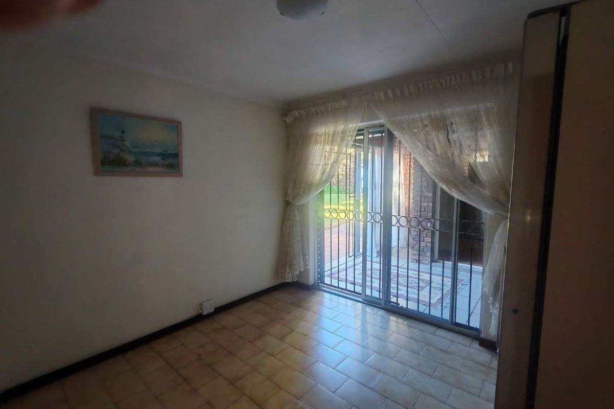 A vacant living room featuring tiled flooring and a sliding glass door with security gate, providing direct access to the outdoor patio area.