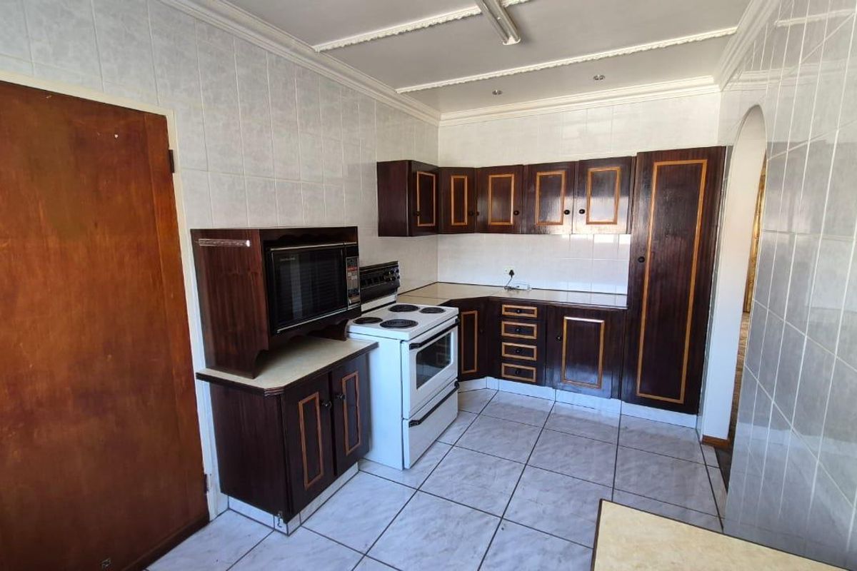 A dated kitchen featuring dark wood cabinetry, tiled walls, and tiled flooring, equipped with a freestanding stove and built-in microwave housing.