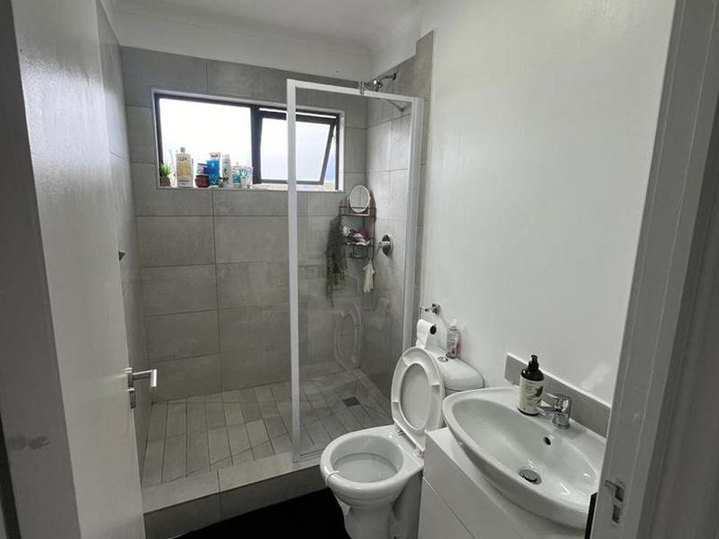 A modern bathroom featuring a walk-in shower with glass screen, a white vanity cabinet with basin, and neutral floor-to-ceiling tiling.