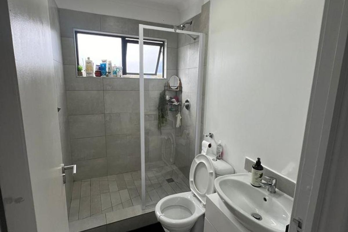 A modern bathroom featuring a walk-in shower with glass screen, a white vanity cabinet with basin, and neutral floor-to-ceiling tiling.