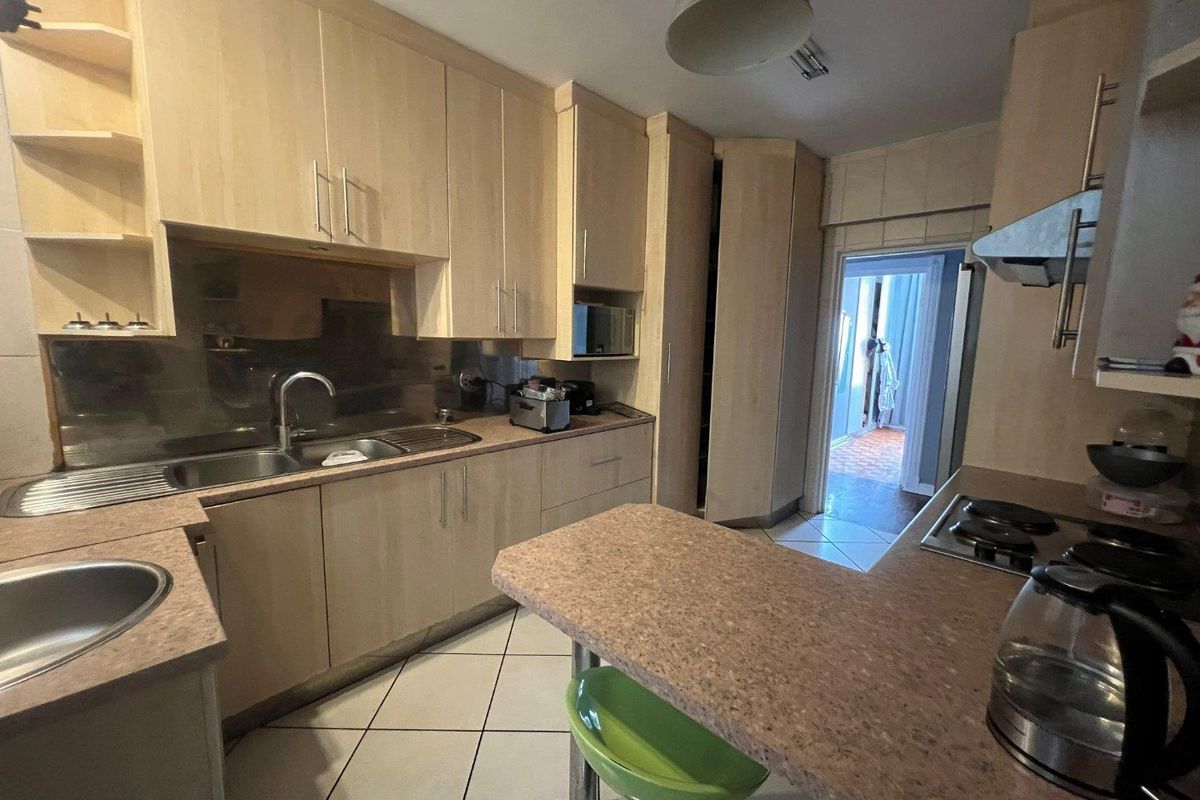 A functional kitchen featuring light wood-tone cabinetry, stone-look laminate countertops, a stainless steel sink, and a built-in hob with an extractor fan.