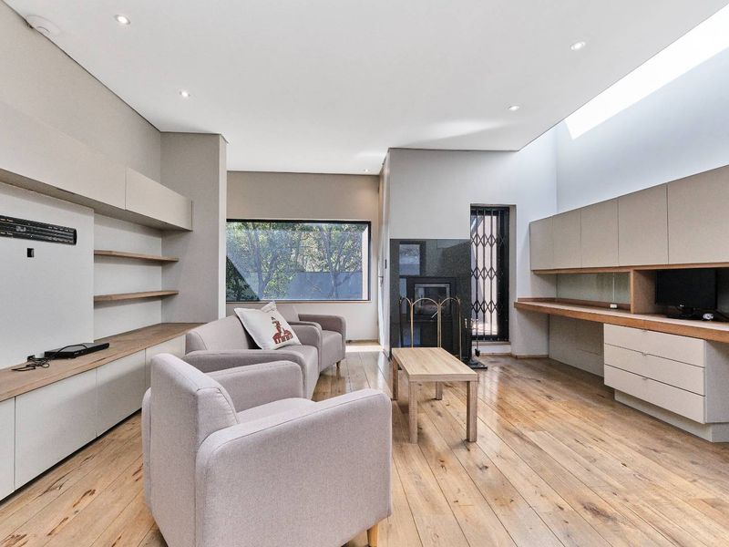 Modern living room featuring hardwood flooring, extensive built-in cabinetry, a fireplace, and a skylight providing ample natural light.