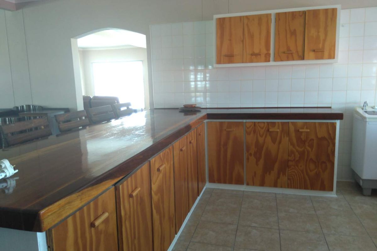A dated kitchen featuring wooden cabinetry, tiled backsplash, and a wooden breakfast bar counter, offering potential for a modern renovation.