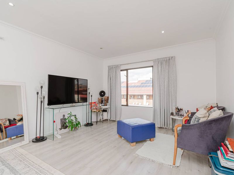A bright living room featuring light-toned laminate flooring, recessed downlighting, and coved cornicing, offering a clean and neutral foundation for the space.