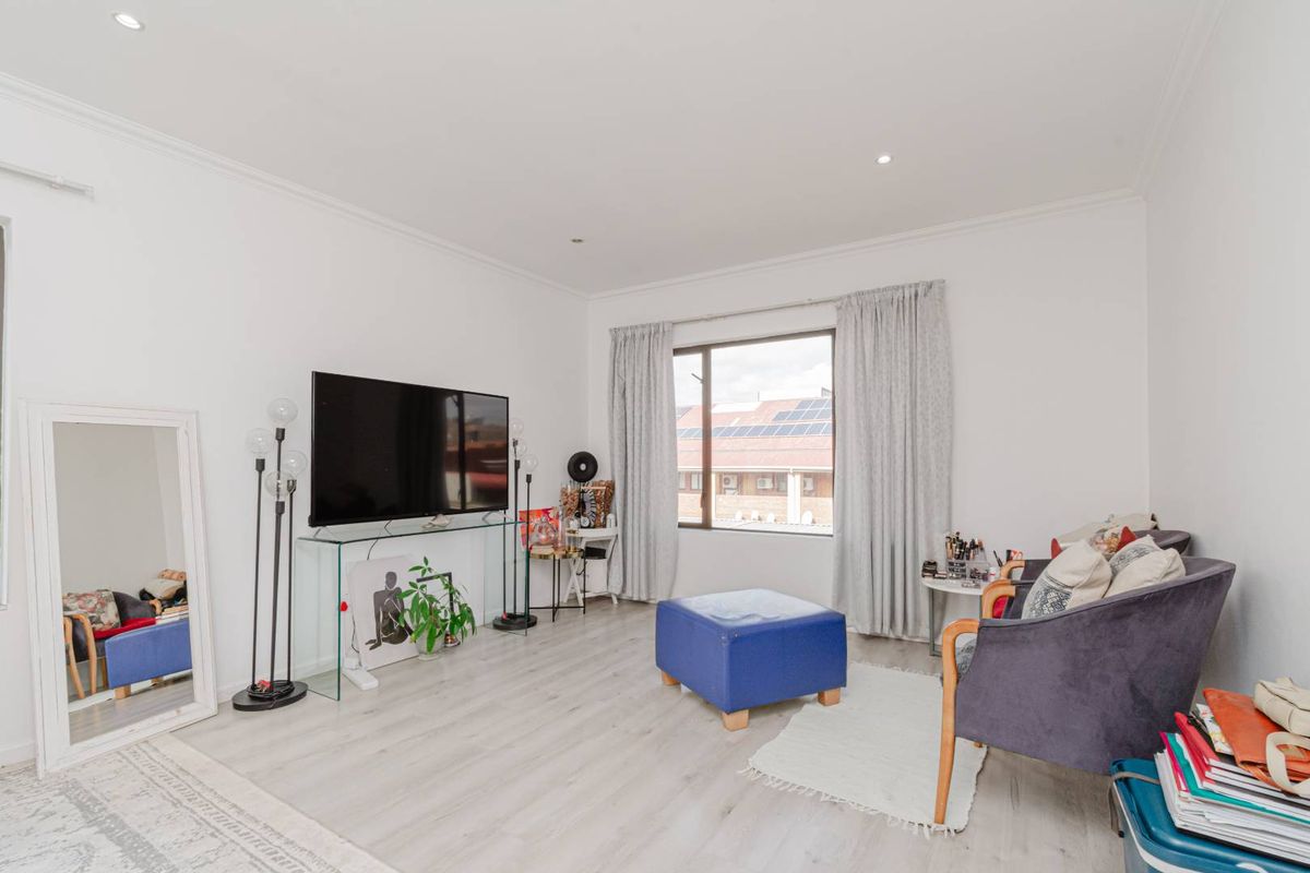 A bright living room featuring light-toned laminate flooring, recessed downlighting, and coved cornicing, offering a clean and neutral foundation for the space.