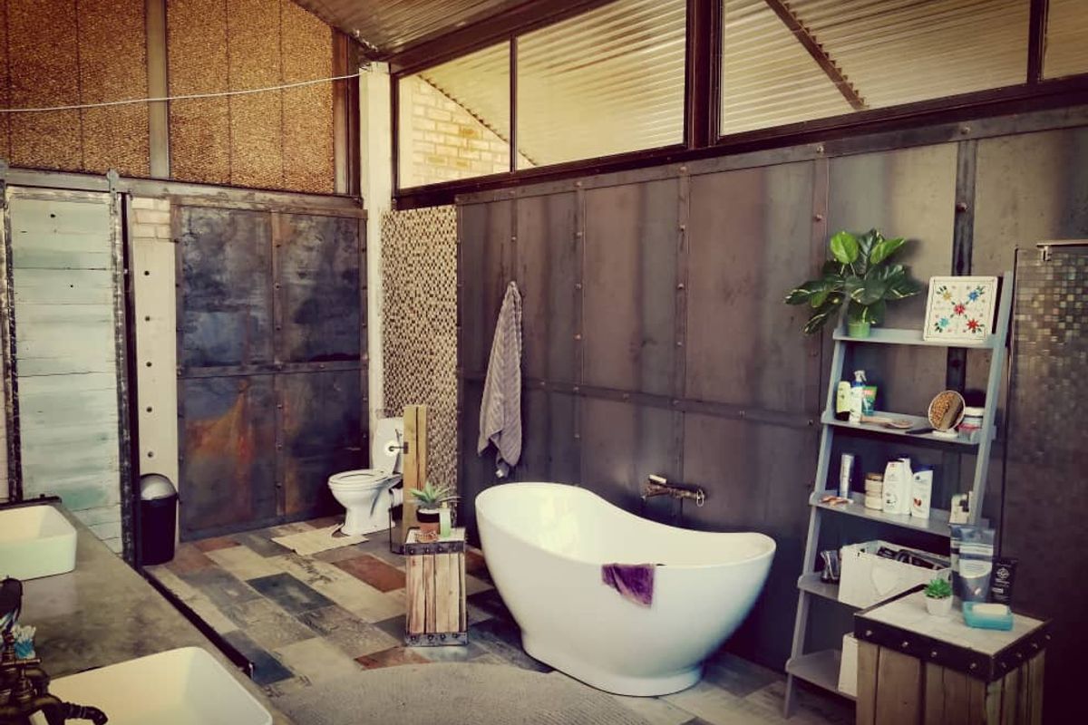 Industrial-style bathroom featuring a freestanding bathtub, dual vessel sinks, metal wall paneling, and unique textured finishes.