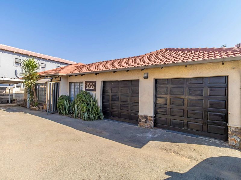 Front exterior view of the property featuring a double garage with dark doors, tiled roof, and stone cladding accents on a paved driveway.