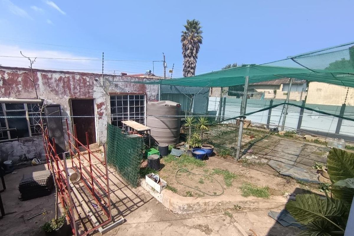 Rear yard area featuring a water storage tank, shade netting structure, and perimeter electric fencing, requiring maintenance to the exterior walls and paving.