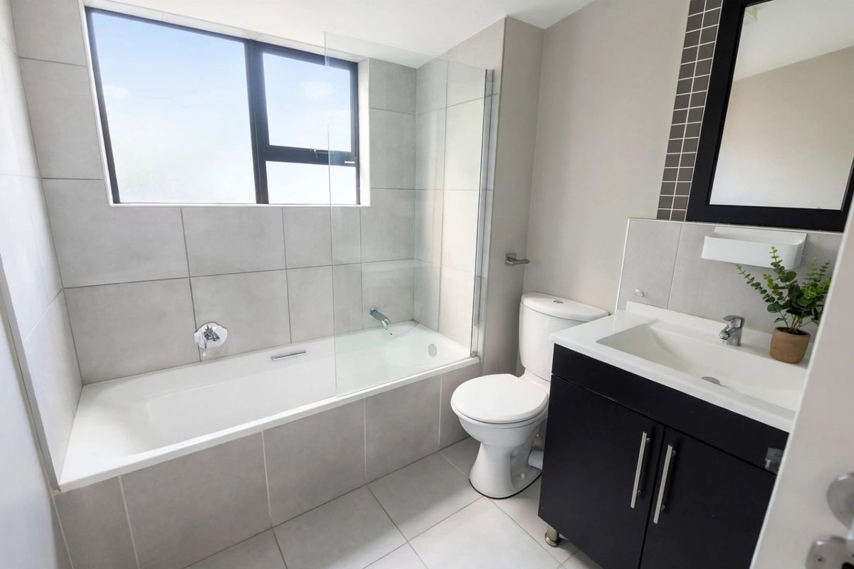 A modern, well-maintained bathroom featuring a bathtub with a glass screen, a vanity unit with a basin, and neutral floor-to-ceiling tiling.