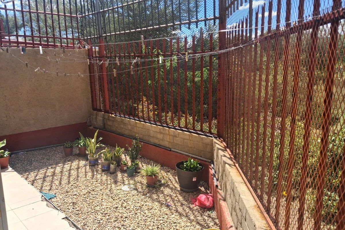 A small, gravel-surfaced outdoor courtyard area enclosed by high metal security fencing and a perimeter wall.