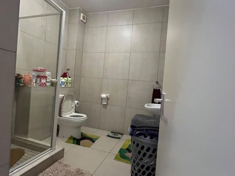 A functional bathroom featuring a glass-enclosed shower, wall-mounted basin, and neutral floor-to-ceiling tiling.