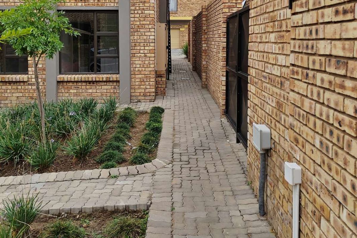 A side walkway featuring face brick walls, paved pathways, and a small landscaped garden area between apartment units.