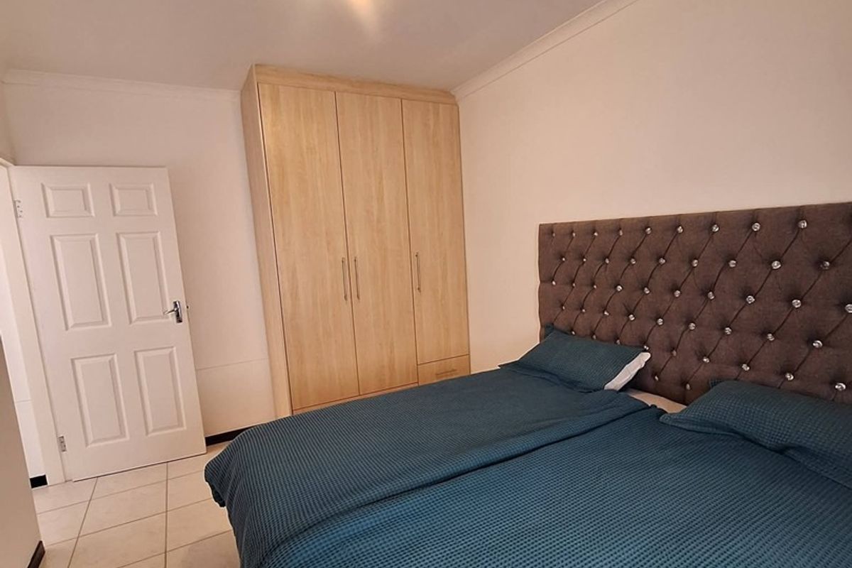 A well-maintained bedroom featuring neutral tiled flooring, a built-in wooden wardrobe, and a classic panel door.
