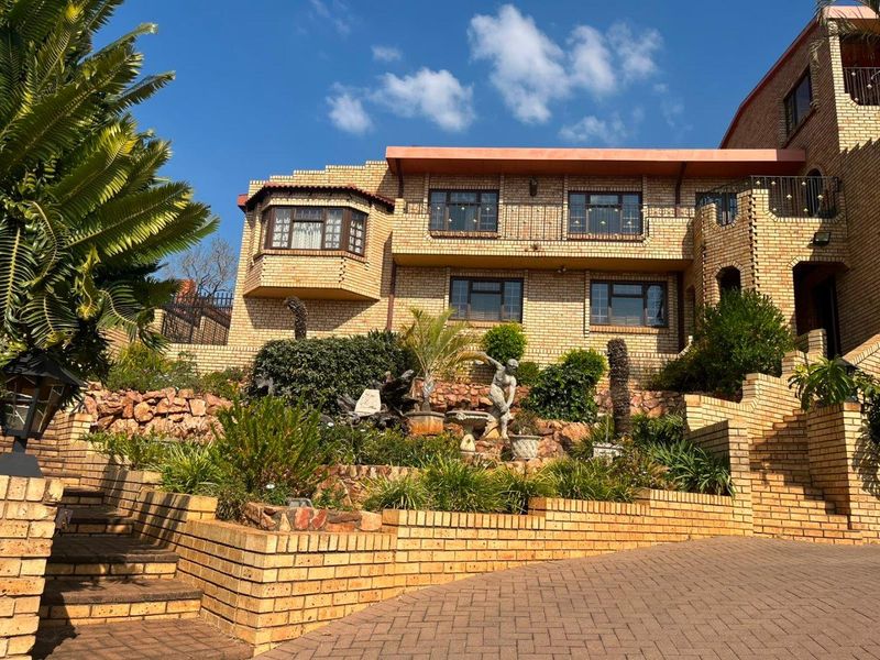 A multi-level face brick residence featuring a paved driveway, tiered garden retaining walls, and a prominent bay window on the upper level.