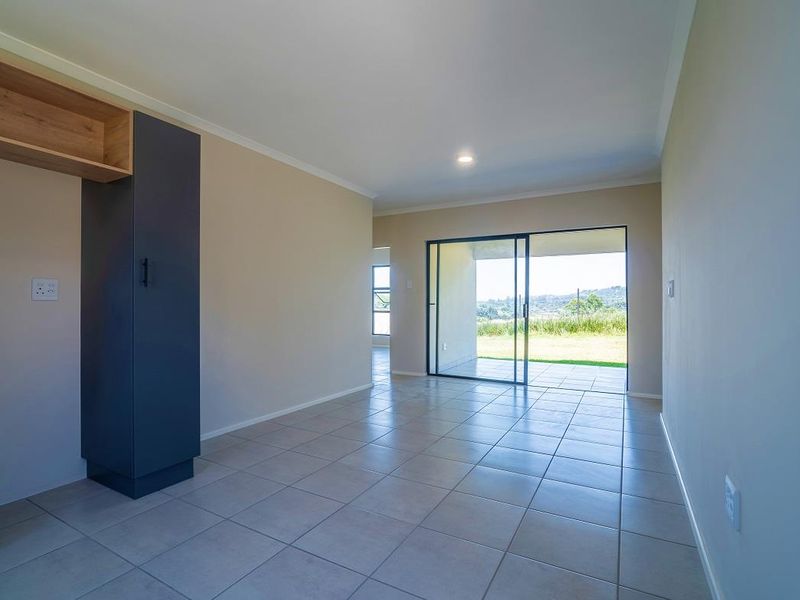 Bright open-plan living area featuring neutral tiled flooring, modern built-in cabinetry, and large sliding glass doors leading to an outdoor patio.