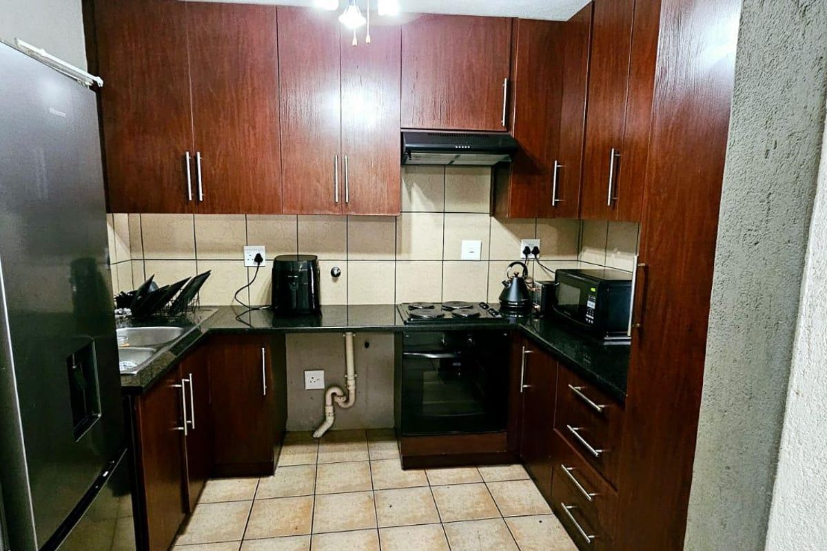 Compact kitchen featuring dark wood cabinetry, granite countertops, built-in oven, hob, extractor fan, and tiled backsplash.