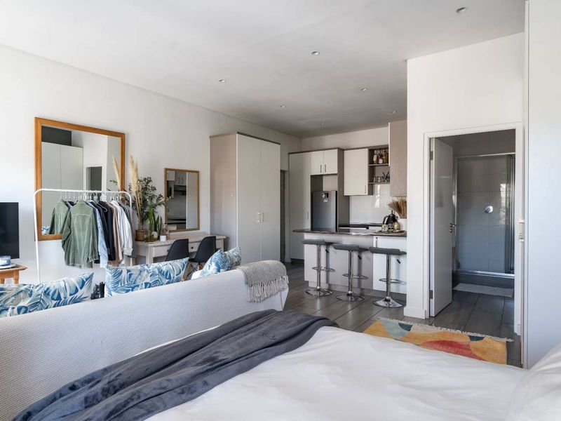 Open-plan studio apartment featuring a modern kitchen with island, tiled flooring, and an adjoining bathroom with a glass-enclosed shower.