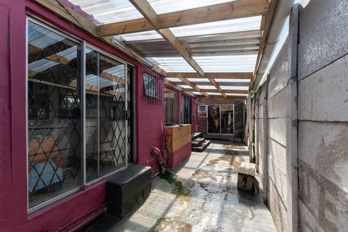 A narrow rear exterior area featuring a covered patio with a timber and polycarbonate roof, concrete paving, and access to the main dwelling.