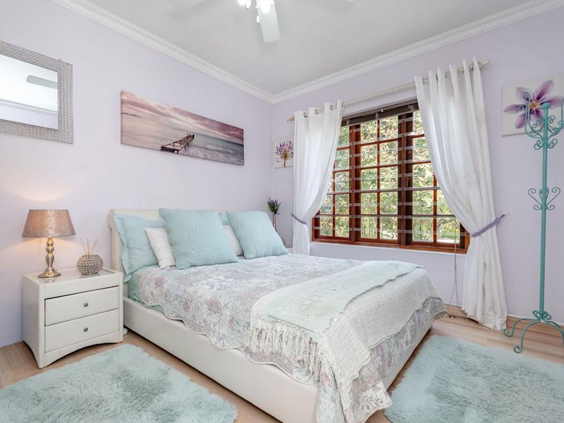 A cozy bedroom featuring laminate flooring, crown molding, a ceiling fan, and a large wooden-framed window allowing natural light.