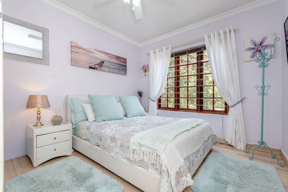 A cozy bedroom featuring laminate flooring, crown molding, a ceiling fan, and a large wooden-framed window allowing natural light.