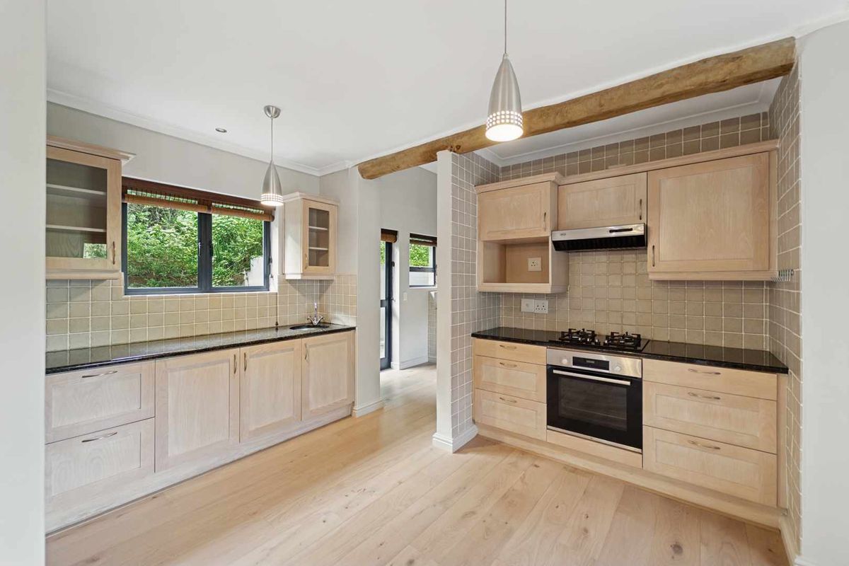 A well-maintained kitchen featuring light wood cabinetry, granite countertops, a gas hob, built-in oven, and an exposed timber ceiling beam.