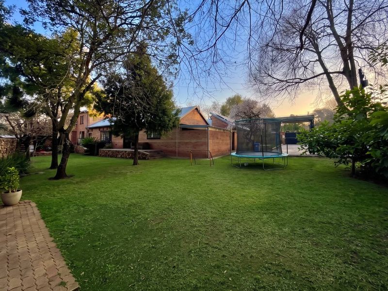 A spacious rear garden featuring a well-maintained lawn, mature trees, and a brick-faced house with a covered patio area.