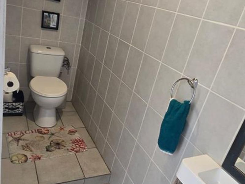 A compact bathroom featuring neutral wall and floor tiling, a modern vanity unit, and a raised toilet platform.