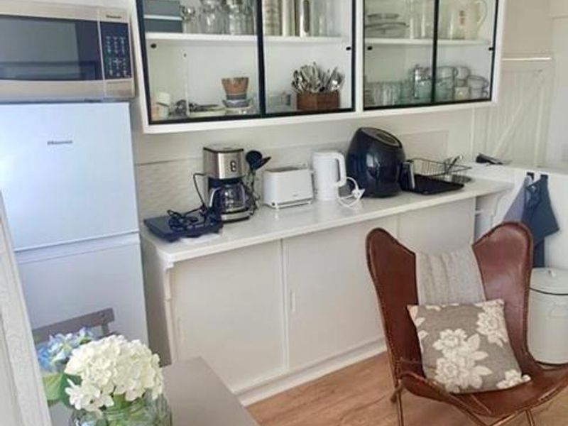 A compact kitchen area featuring white cabinetry with glass-fronted wall units, laminate flooring, and integrated microwave, offering a clean and functional space.
