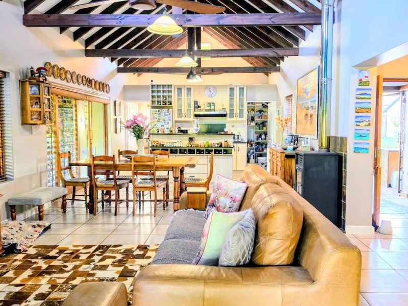 Spacious open-plan living and dining area featuring exposed timber roof trusses, tiled flooring, and a cozy wood-burning fireplace, seamlessly connected to the kitchen.