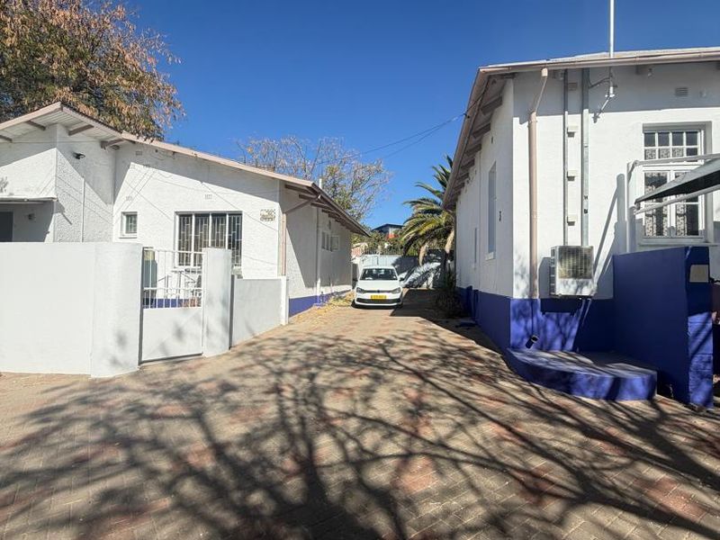 A paved driveway leading between two residential structures, featuring exterior security fixtures and an installed air conditioning unit.