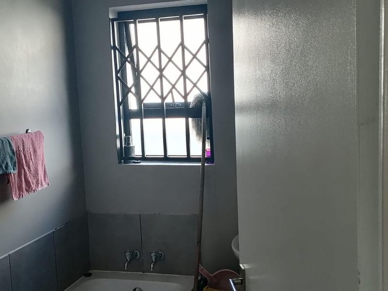 A functional bathroom featuring a bathtub, tiled splashback, and security bars on the window.