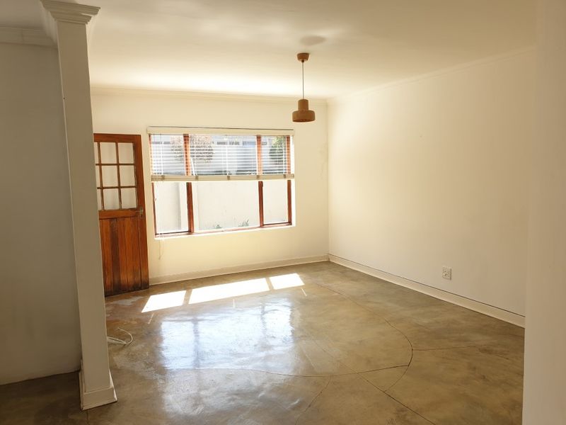 A bright, empty living room featuring polished concrete floors, a timber-framed window, and a classic timber door, offering a clean canvas for interior design.