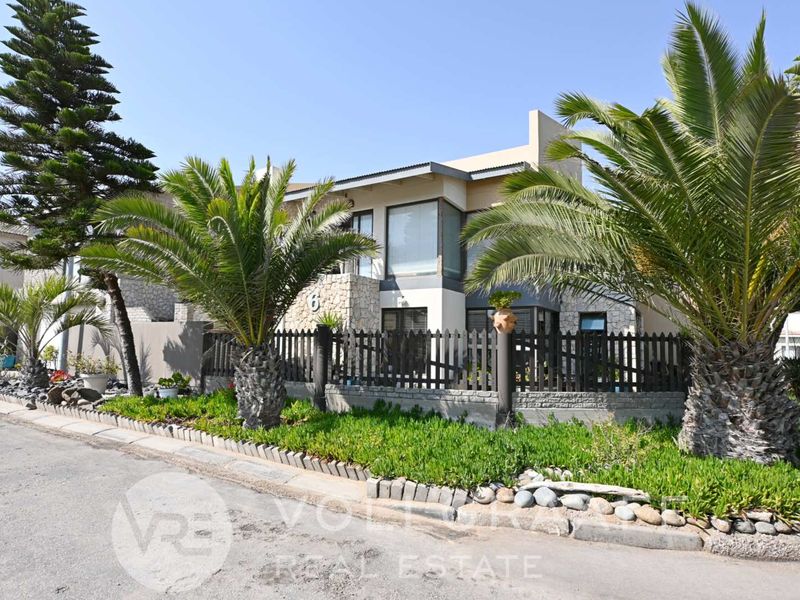 Front elevation of a modern residential property featuring stone cladding, a timber fence, and established palm trees in a landscaped garden setting.