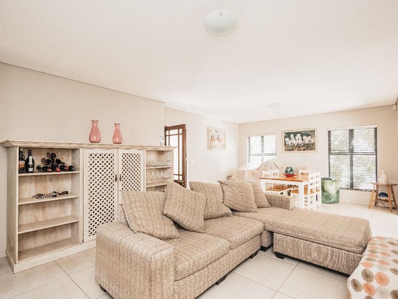 An open-plan living and dining area featuring neutral tiled flooring and large windows with venetian blinds, offering a bright and functional living space.