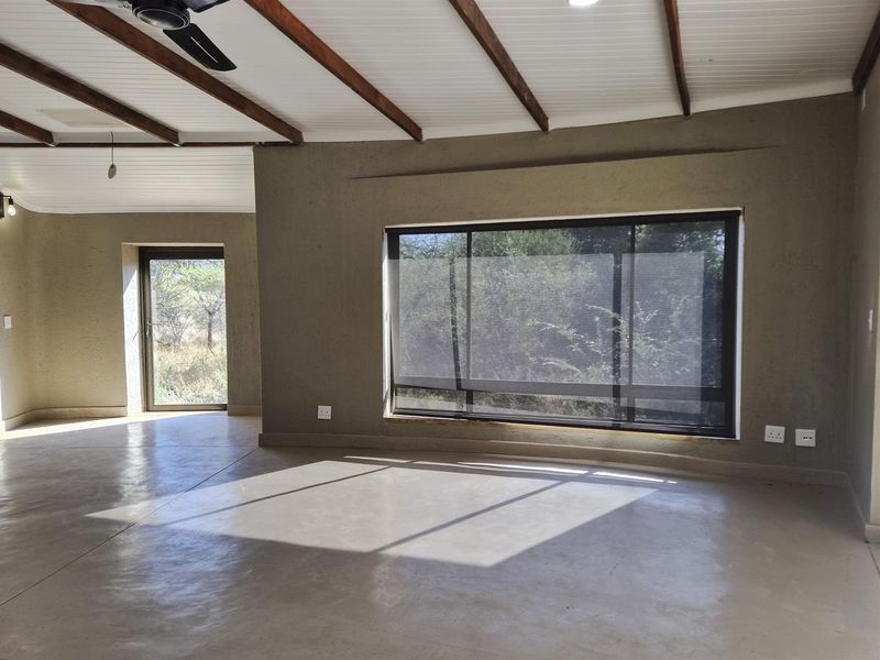 Spacious living area featuring polished concrete floors, exposed timber ceiling beams, and large windows providing natural light and garden views.