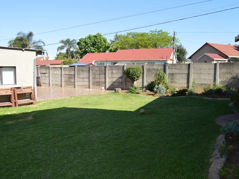A well-maintained rear garden featuring a lush lawn, paved patio area, and secure precast concrete boundary walls.