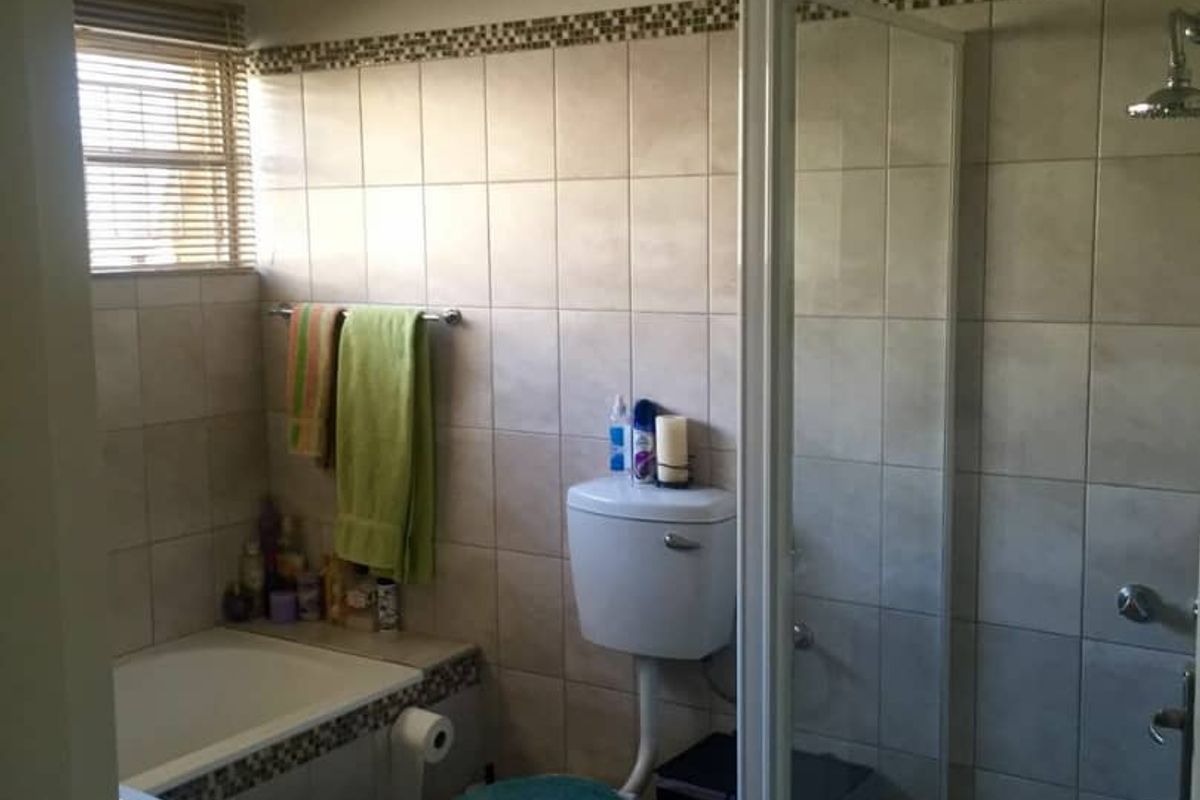 A functional bathroom featuring a tiled shower enclosure, a built-in bathtub, a toilet, and a vanity basin with neutral wall tiling.