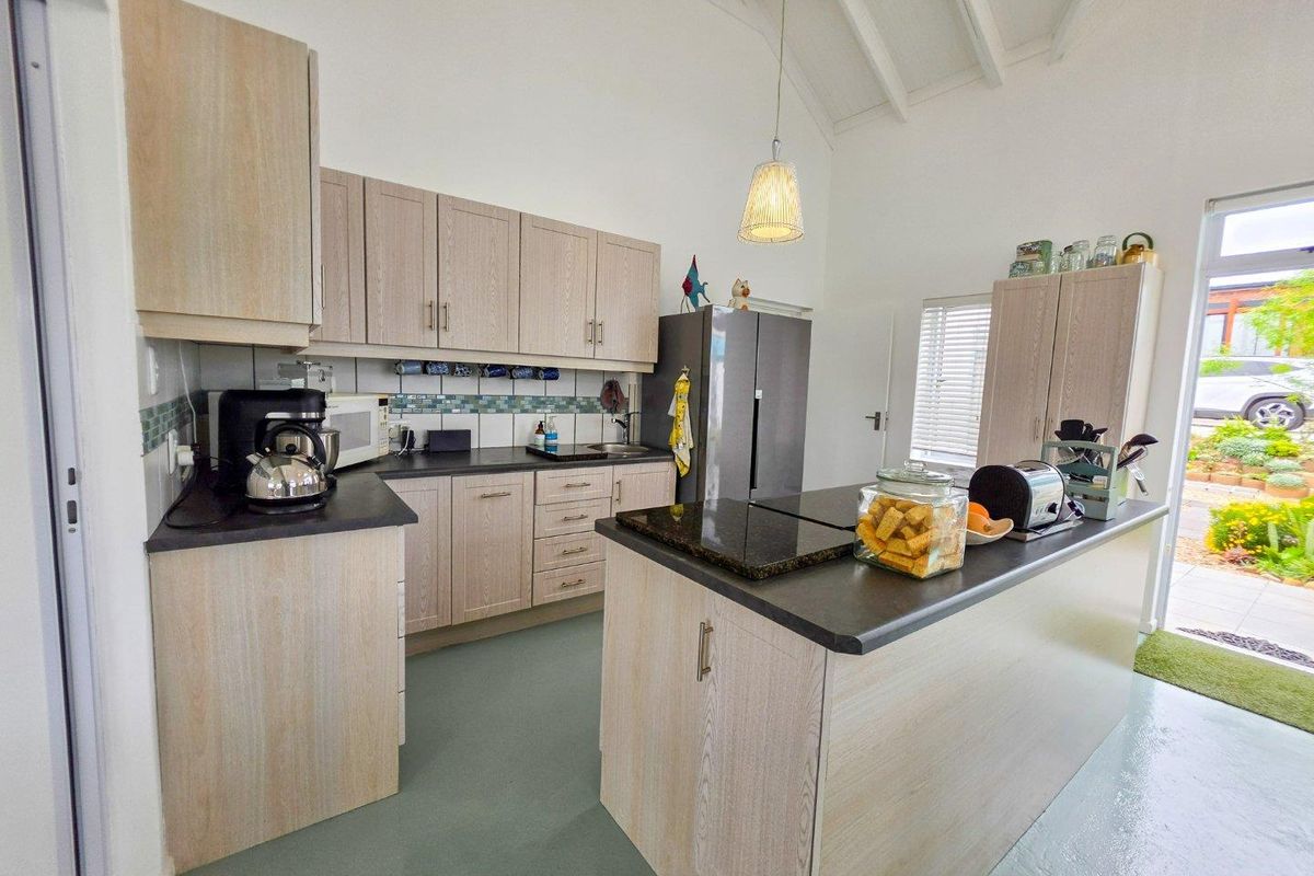 A bright kitchen featuring light wood-tone cabinetry, a central island with dark countertops, a tiled backsplash, and a high vaulted ceiling.