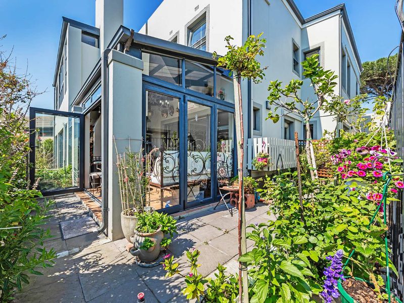 A well-maintained rear exterior view featuring a paved patio area with modern aluminium-framed glass doors leading into the residence.