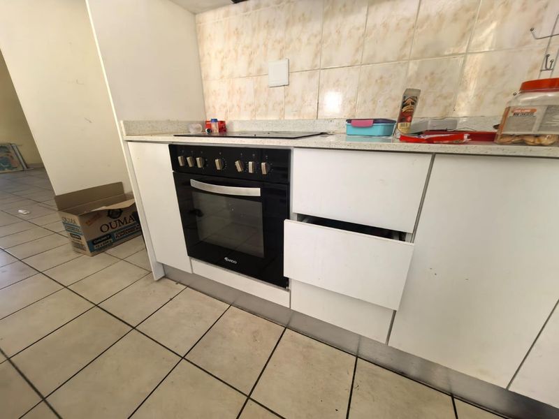 A functional kitchen area featuring a built-in oven, electric hob, tiled backsplash, and base cabinetry, currently showing signs of wear and maintenance needs.