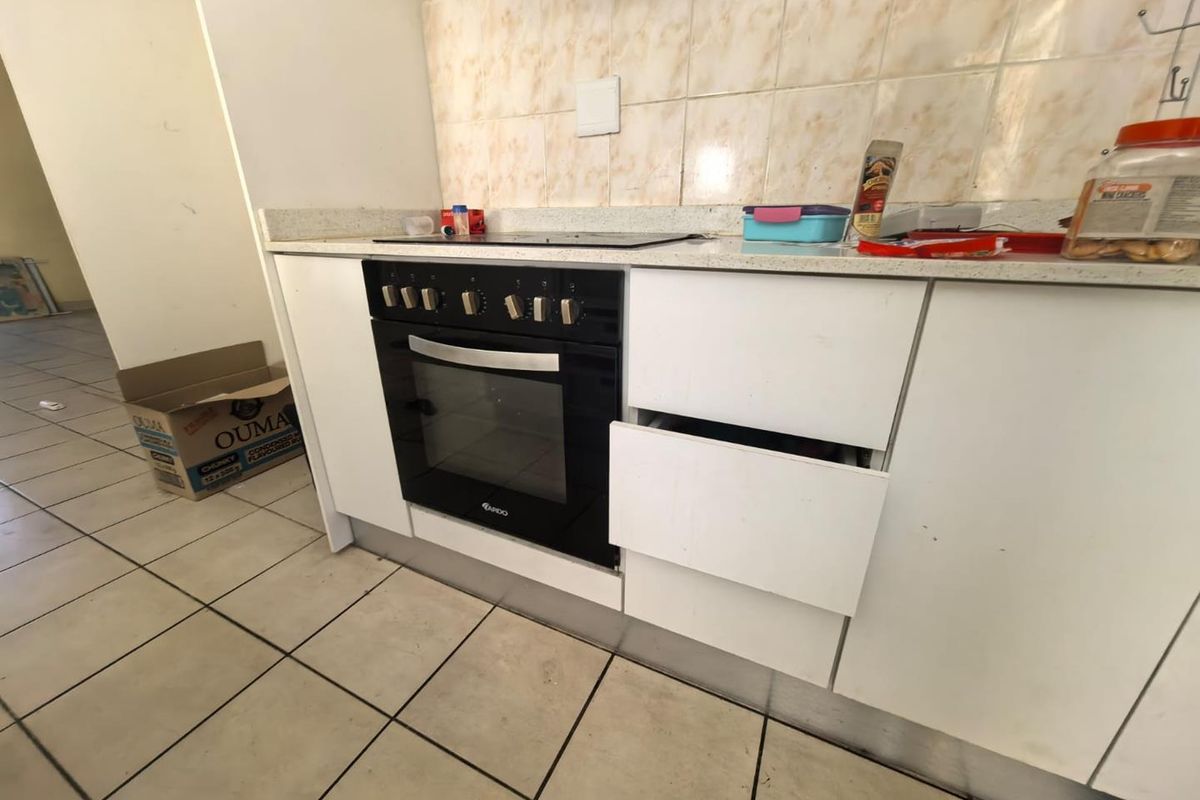 A functional kitchen area featuring a built-in oven, electric hob, tiled backsplash, and base cabinetry, currently showing signs of wear and maintenance needs.