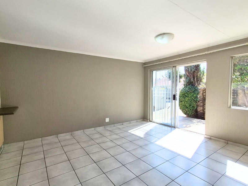 An open-plan living area featuring tiled flooring, kitchen cabinetry, and a sliding glass door providing access to the outdoor space.