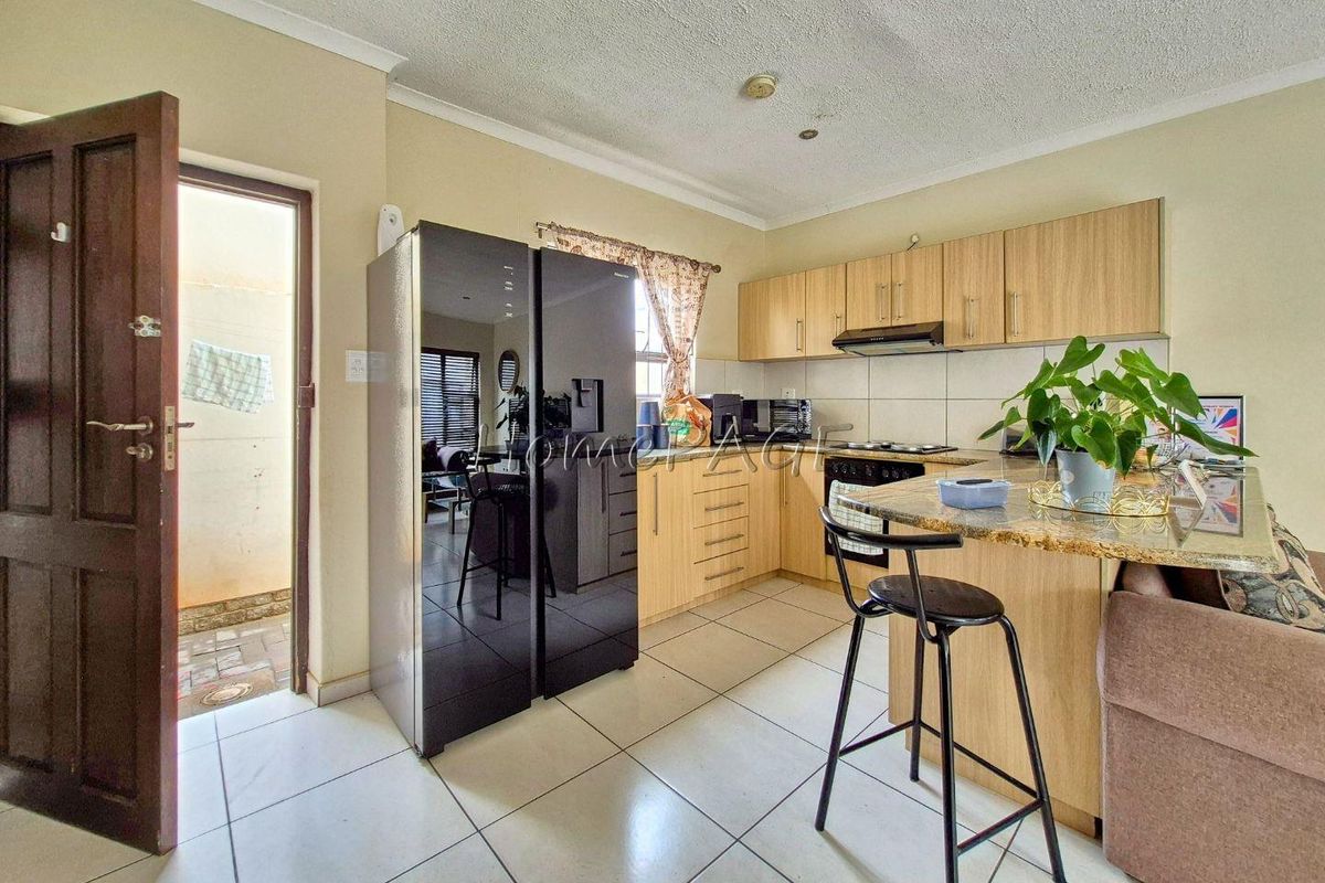 A functional kitchen featuring light wood cabinetry, granite countertops, a breakfast bar, and tiled flooring, with direct access to an outdoor area.
