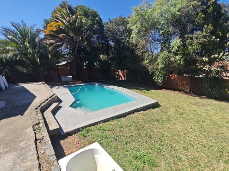 Outdoor pool area featuring a swimming pool with stone coping, concrete patio space, and a surrounding garden with mature trees and brick boundary walls.