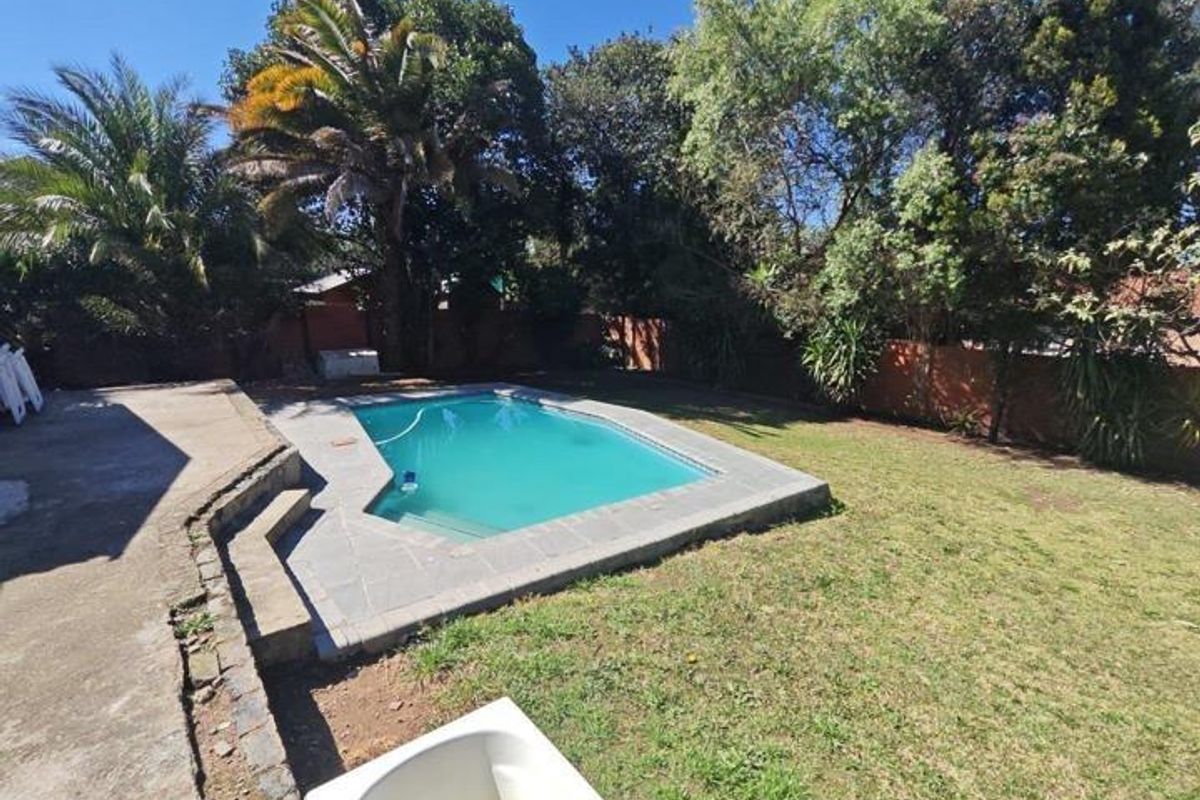 Outdoor pool area featuring a swimming pool with stone coping, concrete patio space, and a surrounding garden with mature trees and brick boundary walls.