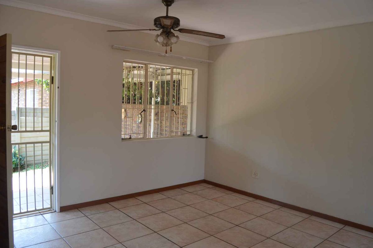 An empty living room featuring tiled flooring, a ceiling fan, and security bars on the window and door.